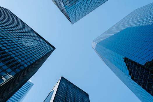 Low angle of high business towers with glass mirrored windows located in megalopolis downtown against blue sky